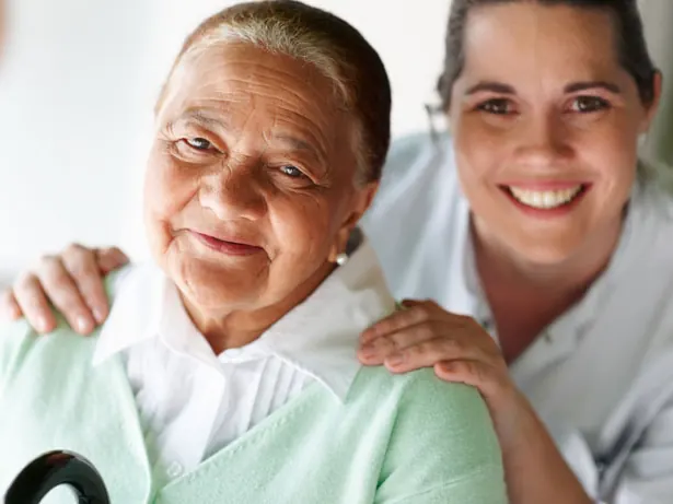 Cuidadora sorridente abraçando uma senhora idosa pelos ombros
